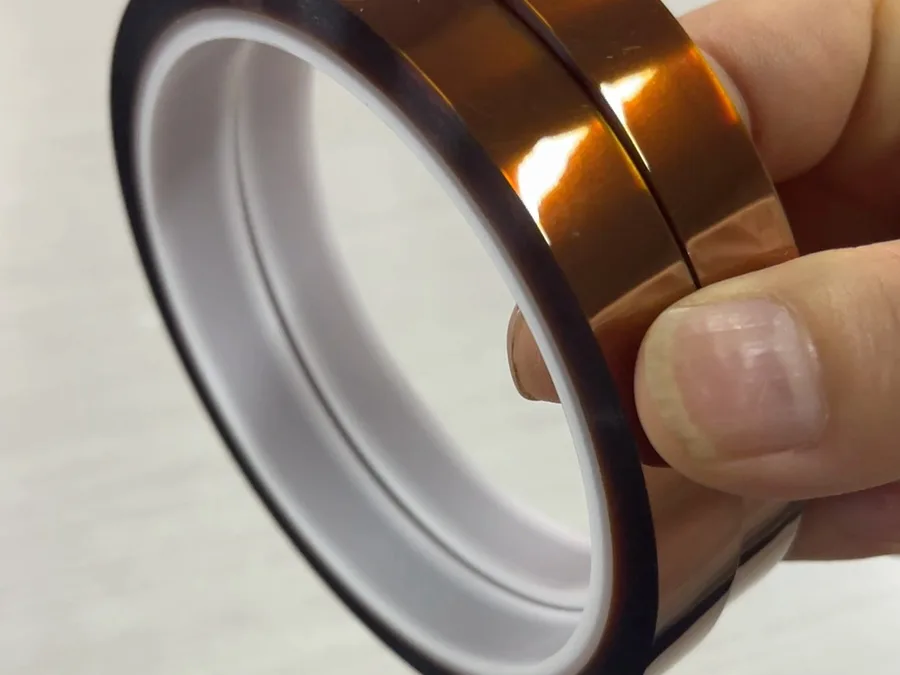 A hand holding a roll of amber polyimide tape